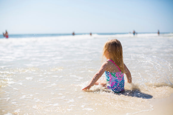 little girl sitting on the beach in a swimsuit